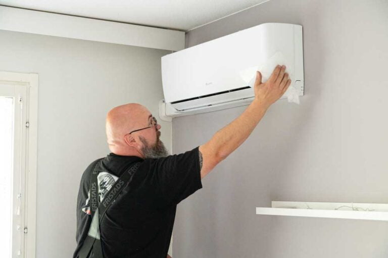 Tehotikka asentamassa ilmalämpöpumpun sisäyksikköä makuuhuoneen seinään.