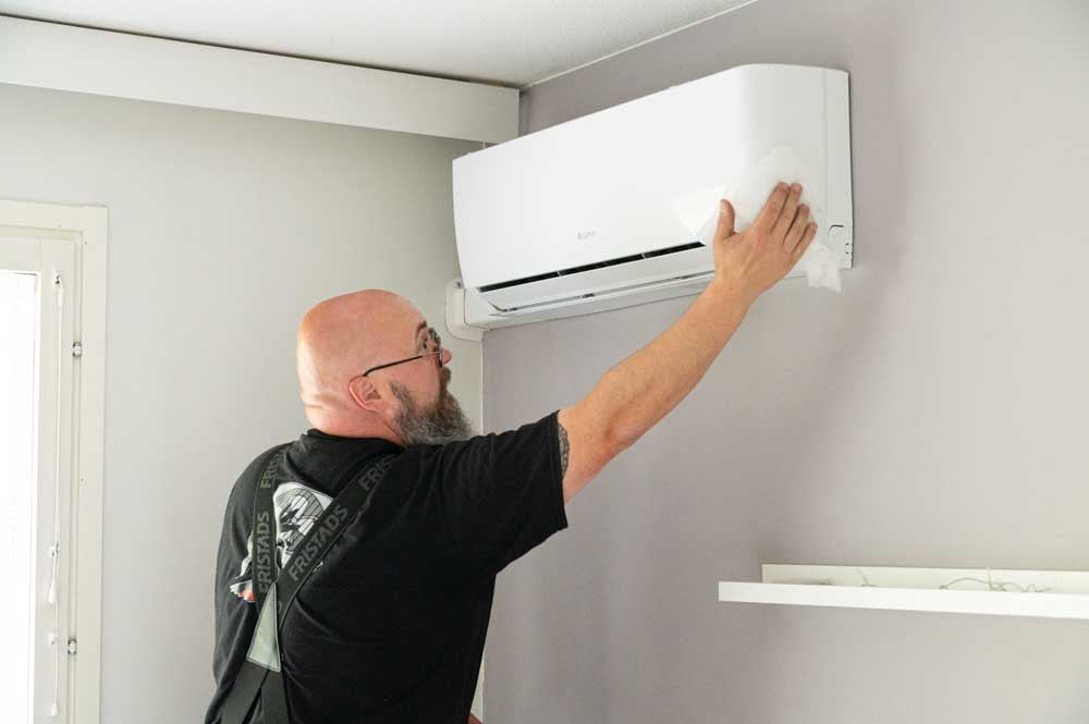 Tehotikka asentamassa ilmalämpöpumpun sisäyksikköä makuuhuoneen seinään.